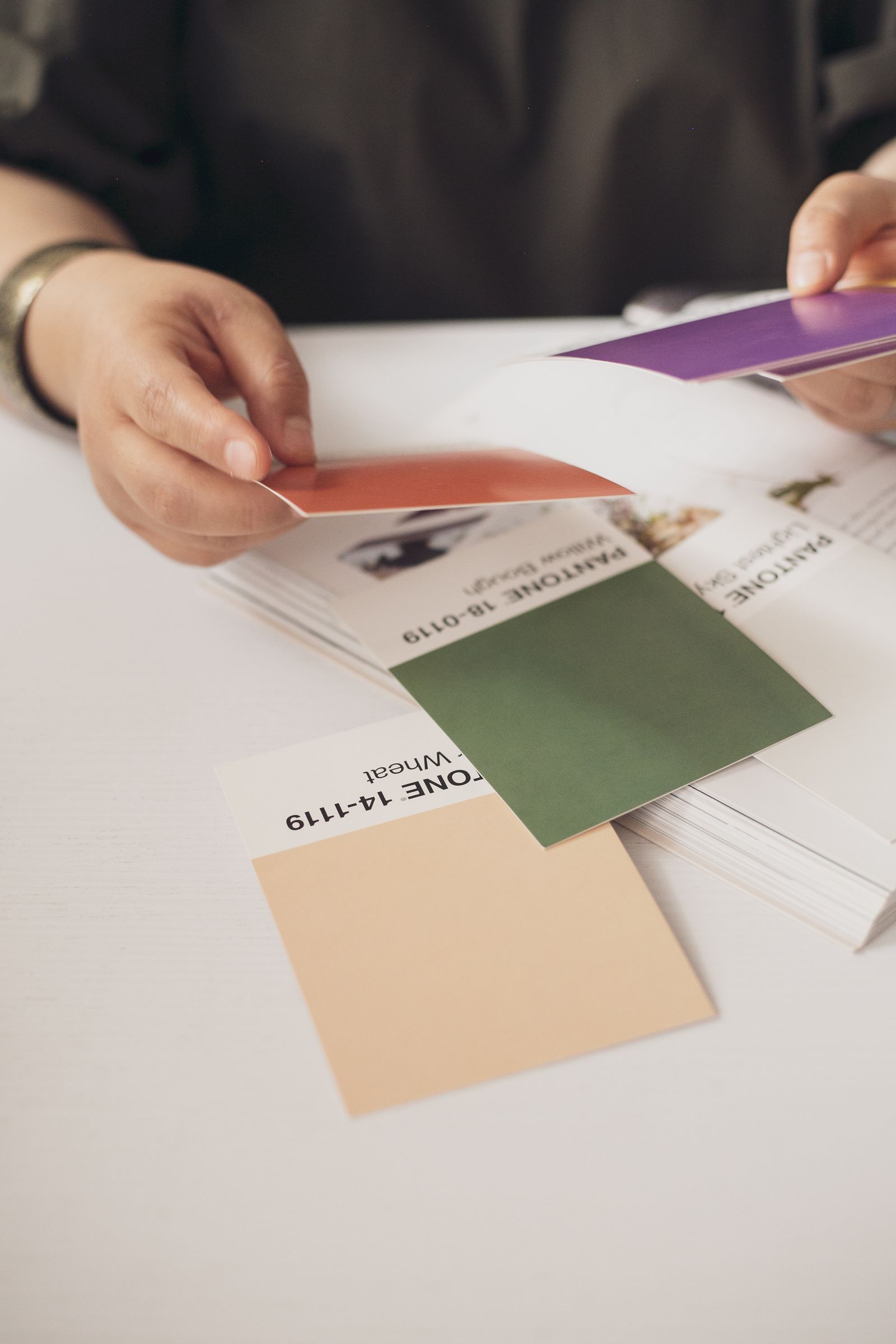 Hände wählen Farbmuster über einem Tisch mit Papiermustern aus